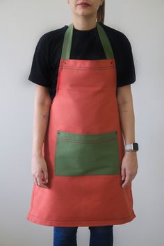 a woman wearing an orange and green apron with two pockets on the front, standing against a white wall