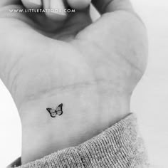 a small butterfly tattoo on the left inner wrist, which is also in black and white