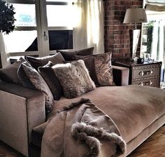 a couch with pillows and blankets on top of it in front of a brick wall