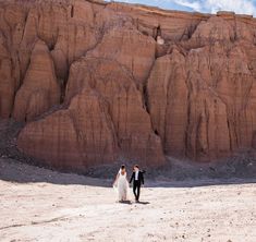 a bride and groom walking through the desert