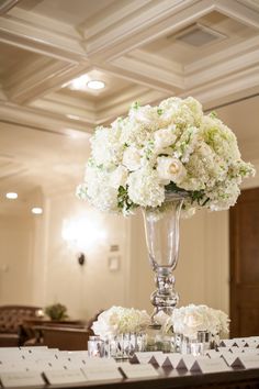 a tall vase filled with white flowers sitting on top of a table next to chairs