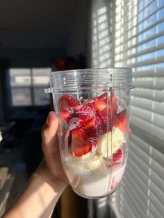 a person holding up a blender with strawberries and bananas in it's cup