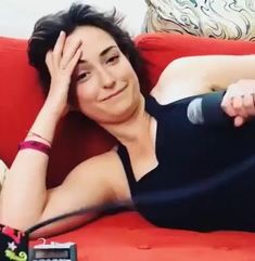 a woman laying on top of a red couch next to a phone and remote control