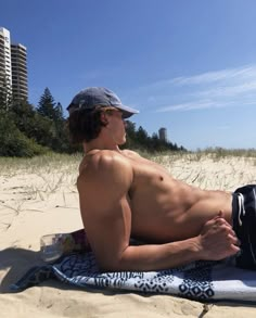 a shirtless man laying on top of a beach towel next to the ocean with buildings in the background