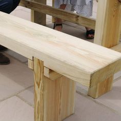 a wooden bench sitting on top of a stone floor next to a person wearing sandals