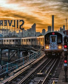 two trains traveling down tracks next to each other in front of a large city skyline