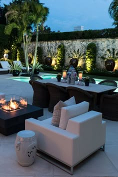 a fire pit sitting in the middle of a patio surrounded by palm trees and chairs