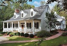 a white house surrounded by trees and grass with lots of windows on the front porch