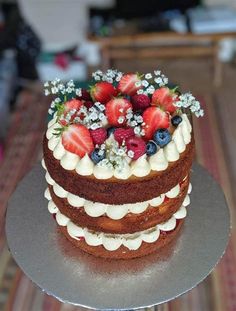 a triple layer cake with strawberries and blueberries on top is sitting on a table