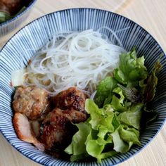 a blue bowl filled with meat, noodles and veggies on top of a wooden table