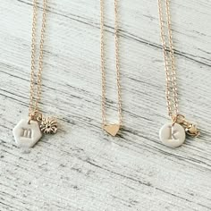 three different necklaces with charms on them sitting on top of a wooden table next to each other