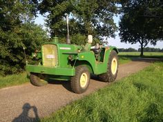 a large green tractor parked on the side of a road next to a lush green field