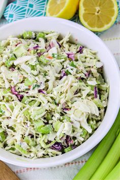 a white bowl filled with coleslaw next to celery and lemon wedges