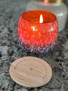 a red candle sitting on top of a table next to a wooden coaster that says, no touch or squeeze