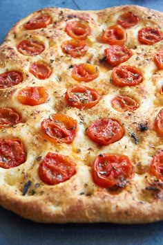 a pizza with tomatoes on it sitting on top of a blue tablecloth next to a fork and knife