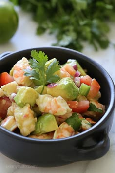 a salad with shrimp, avocado and tomatoes in a black bowl on a table