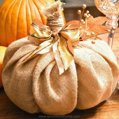 a burlap pumpkin sitting on top of a wooden table next to wine glasses