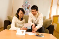 a man and woman sitting on a couch looking at an open christmas card in front of a christmas tree