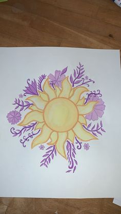 a drawing of a sun surrounded by purple flowers on a white paper with crayons