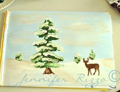 a painting of a deer in the snow next to a pine tree on a table