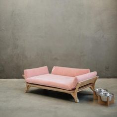 a pink couch sitting on top of a cement floor next to a metal dog bowl