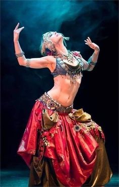 a woman in a red and gold belly dance outfit with her arms out to the side