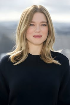 a woman with blonde hair wearing a black sweater and smiling at the camera while standing in front of a cityscape