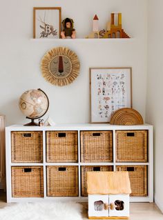 a white dresser with wicker baskets on top and pictures hanging above it, along with other items