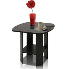 a small table with a vase and a cup on it next to a red flower