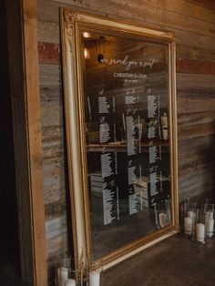 a wedding seating chart in front of a large mirror with candles on the table next to it