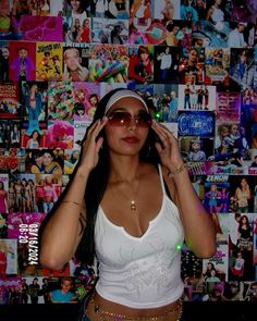 a woman wearing sunglasses and a white tank top is standing in front of a wall covered with posters