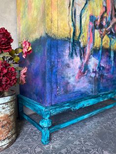 a vase with flowers sitting next to a painted cabinet