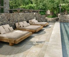 four chaise lounges are lined up next to a swimming pool and stone wall