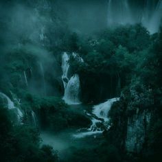 a waterfall in the middle of a forest filled with trees and misty water flowing down it's sides