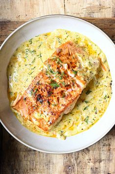 a white plate topped with salmon and grits on top of a wooden table next to a fork