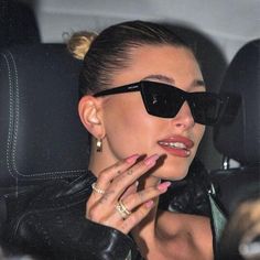 a woman wearing sunglasses sitting in the back seat of a car with her hand on her lip