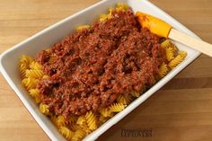 a white bowl filled with pasta and meat sauce on top of a wooden table next to an orange peel