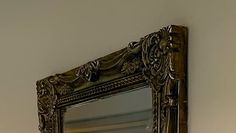 an ornate mirror hanging on the wall above a toilet paper dispenser in a bathroom