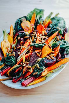 a white plate topped with carrots, beets and spinach salad on top of a wooden table