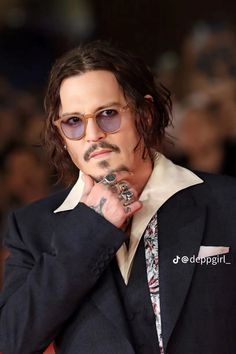 a man with long hair and glasses is posing for the camera while holding his hand to his chin