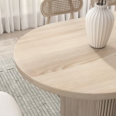 a white vase sitting on top of a wooden table next to two chairs and a rug