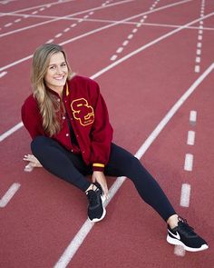 a woman sitting on the side of a running track wearing a red jacket and black leggings