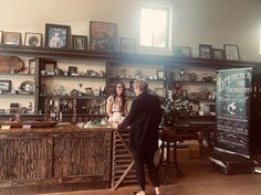 two women standing in front of a counter with shelves full of items on the wall