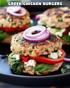 two chicken burgers on a black plate with onions and spinach in the middle