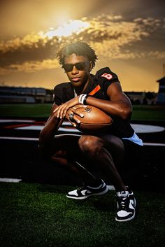 a man kneeling down holding a football on top of a field with the sun in the background