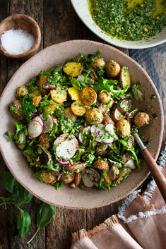 a bowl filled with salad next to two bowls of pesto and other food items