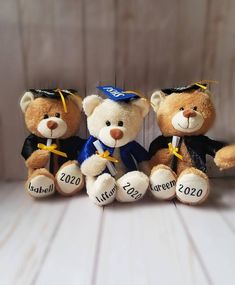 three teddy bears with graduation caps and gowns sitting next to each other on a table