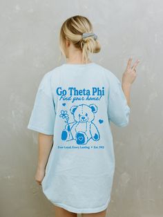 a woman wearing a t - shirt that says go there phi and has a teddy bear on it