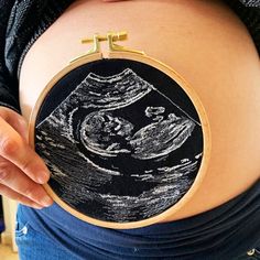 a pregnant woman holding up a black and white drawing on a piece of fabric with gold trim