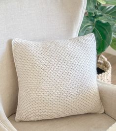 a white cushion sitting on top of a beige chair next to a potted plant